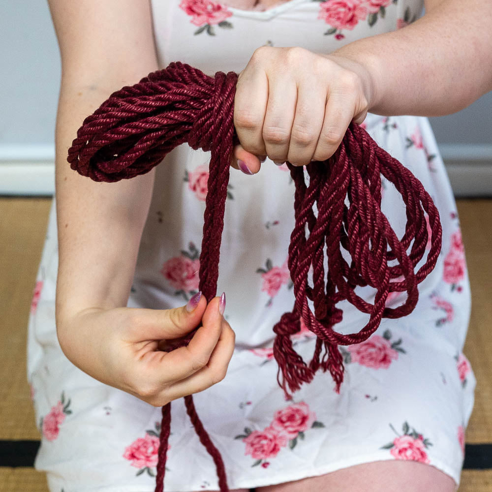 Close up of hands coiling a soft, red jute shibari rope