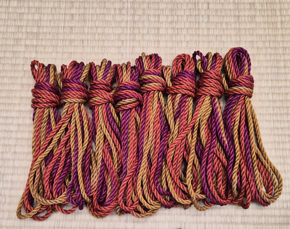 8 hanked shibari ropes, featuring red, burnt orange, and yellow.