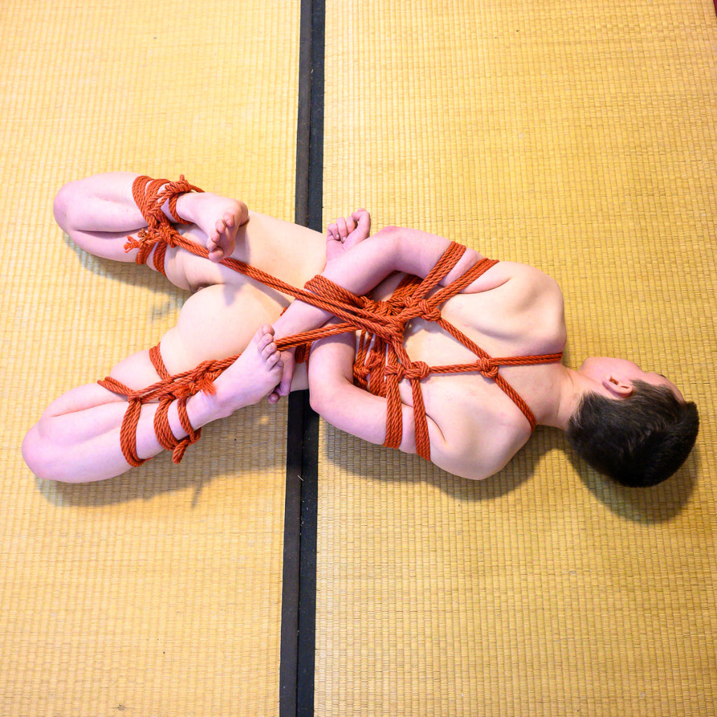 Person bound with orange rope on a yellow tatami mat floor