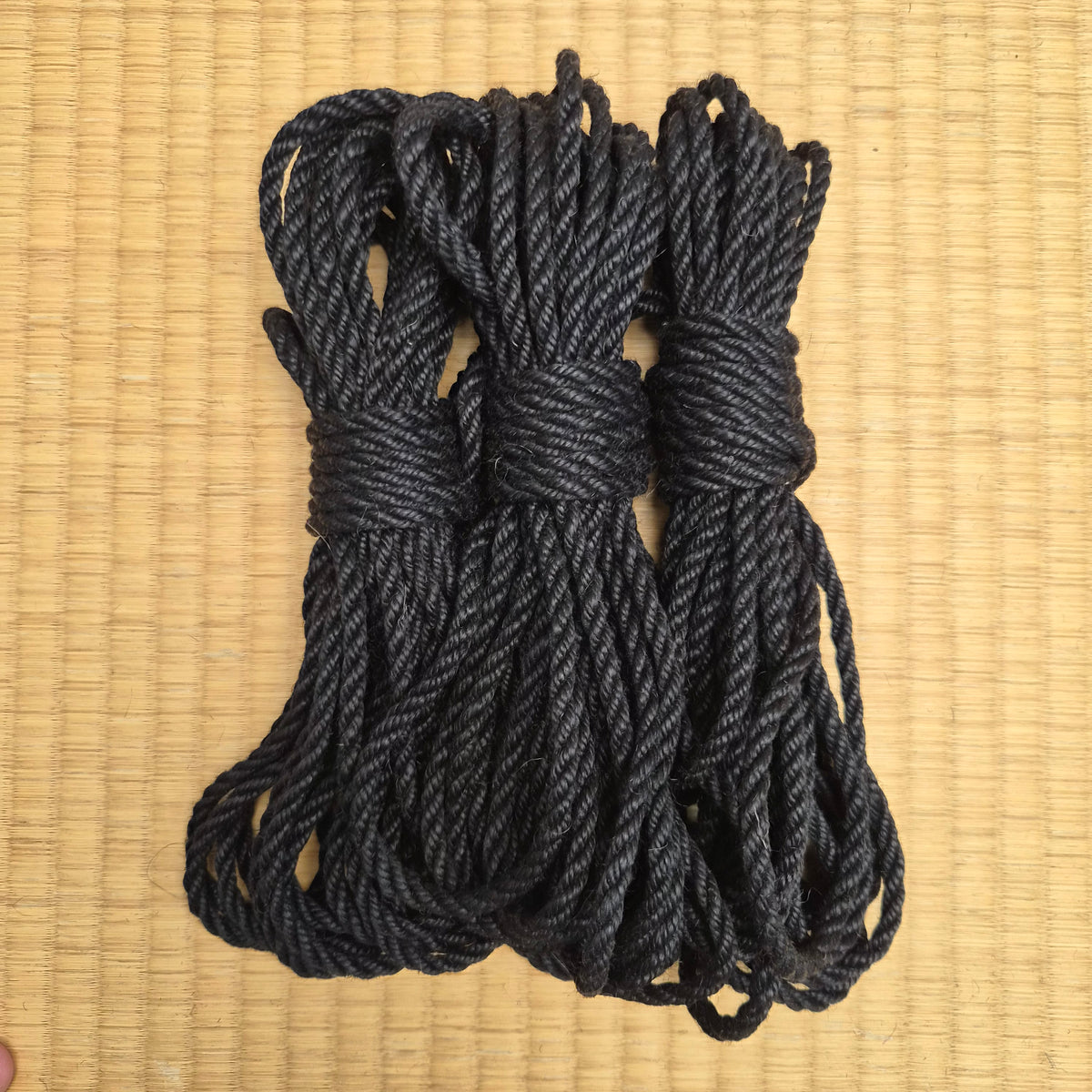 Three coiled bundles of thick black twisted rope tied with simple knots, arranged on a light tan woven mat background.