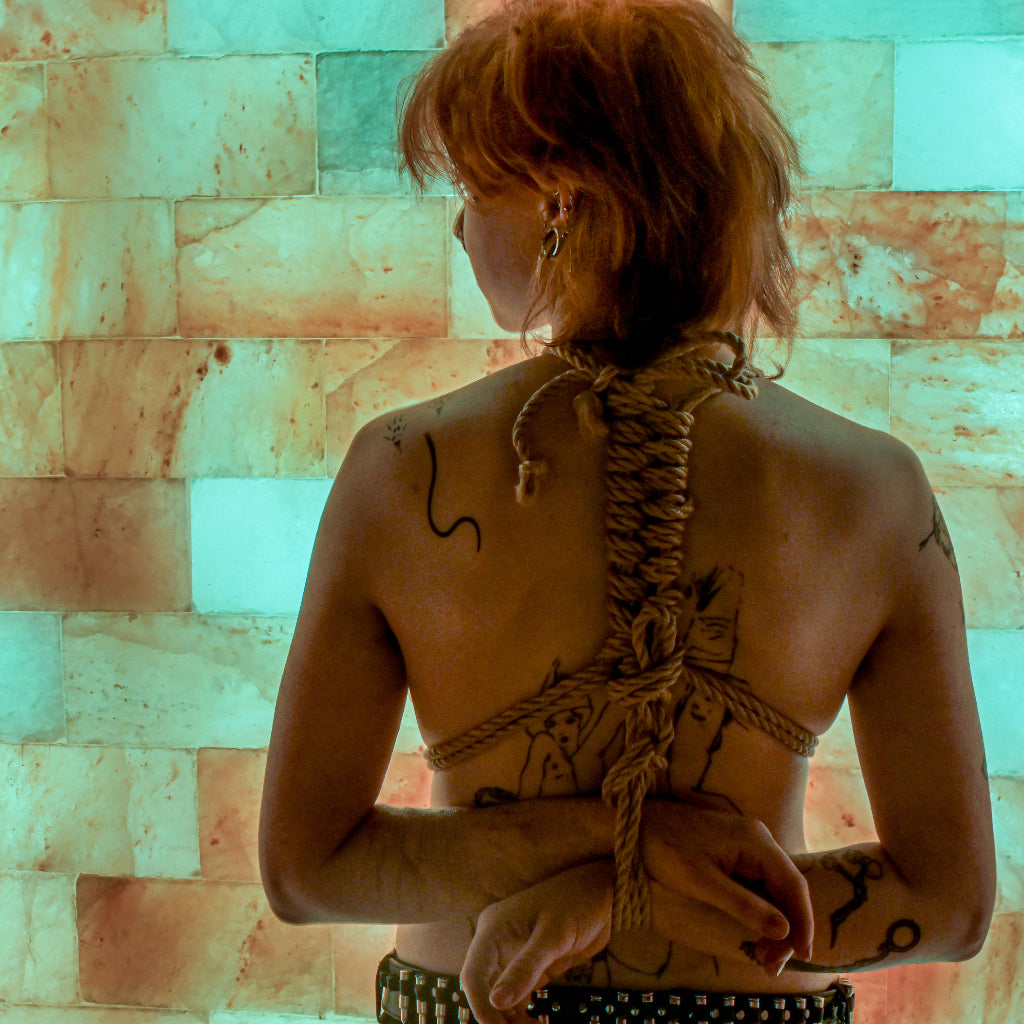 Tattooed women  with hands tied behind back standing in front of salt wall
