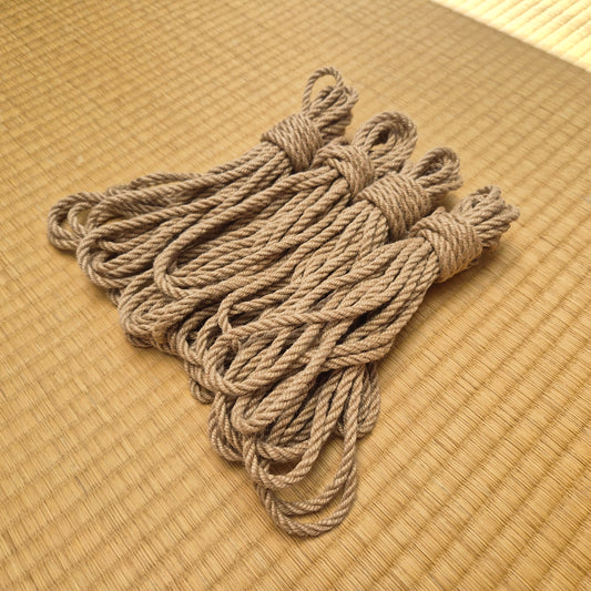 A bundle of 4 natural tan kinbaku ropes tied in hanks, arranged on a woven straw mat background.