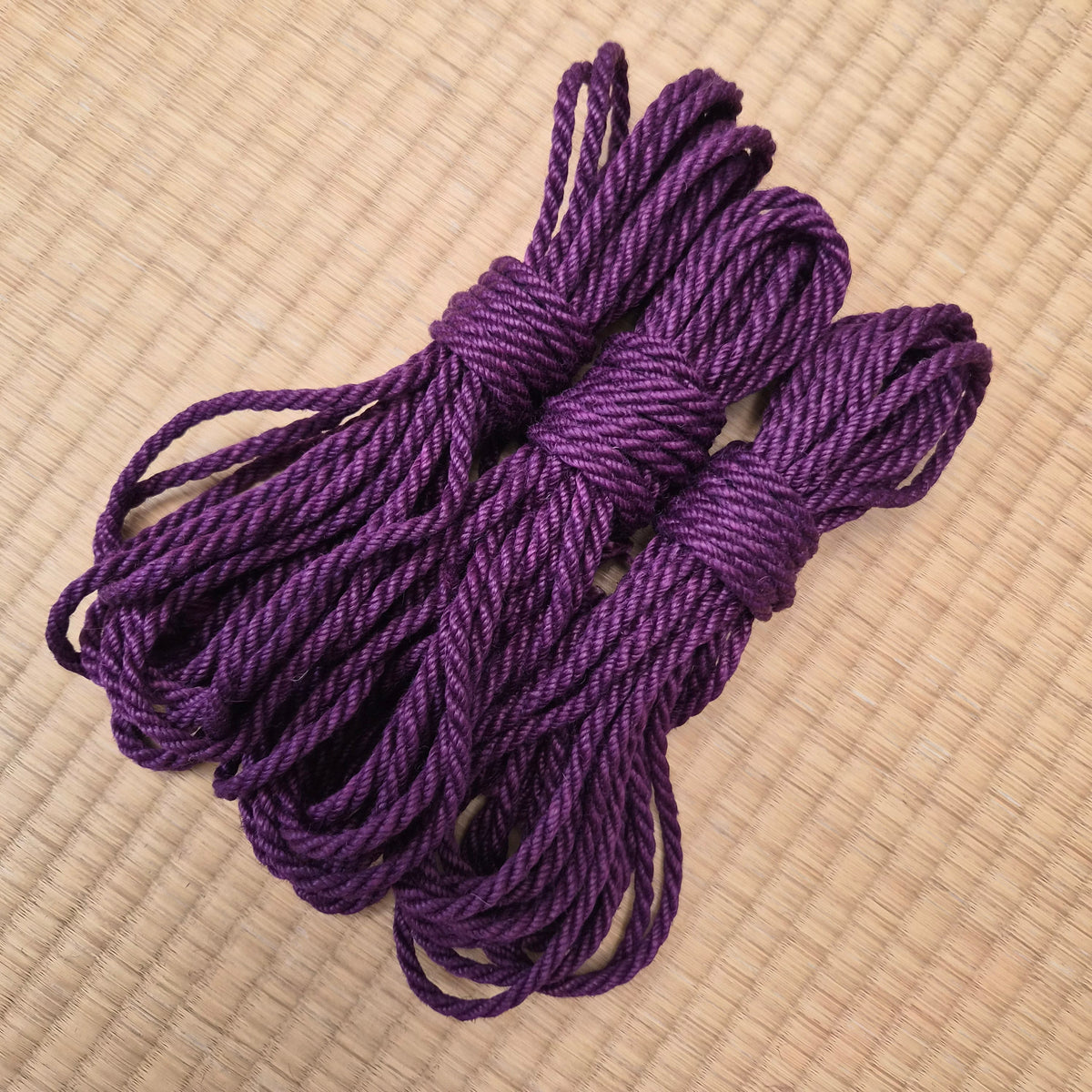 A coiled bundle of thick purple rope or cord placed on a light beige woven mat background.