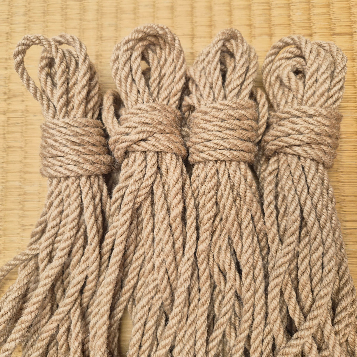Set of Four coiled bundles of natural jute Kinbaku rope tied with knots, arranged side-by-side on a light tan woven mat background.