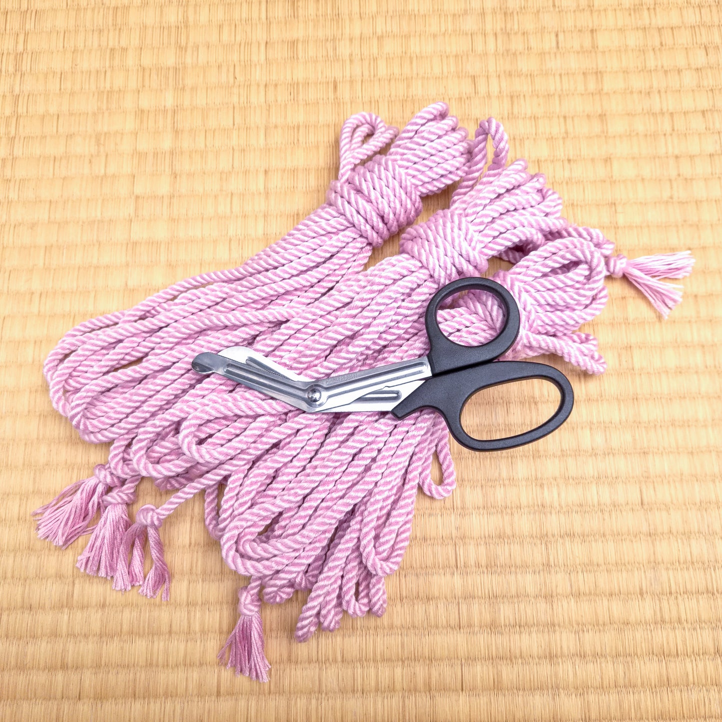 Pink silk rope with black-handled scissors on a beige woven surface