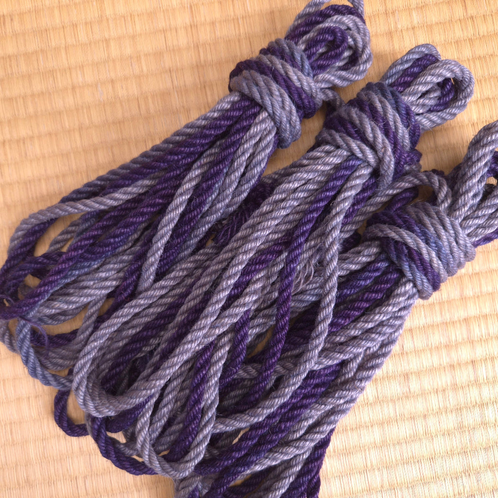 Three skeins of purple and gray shibari rope on a woven surface