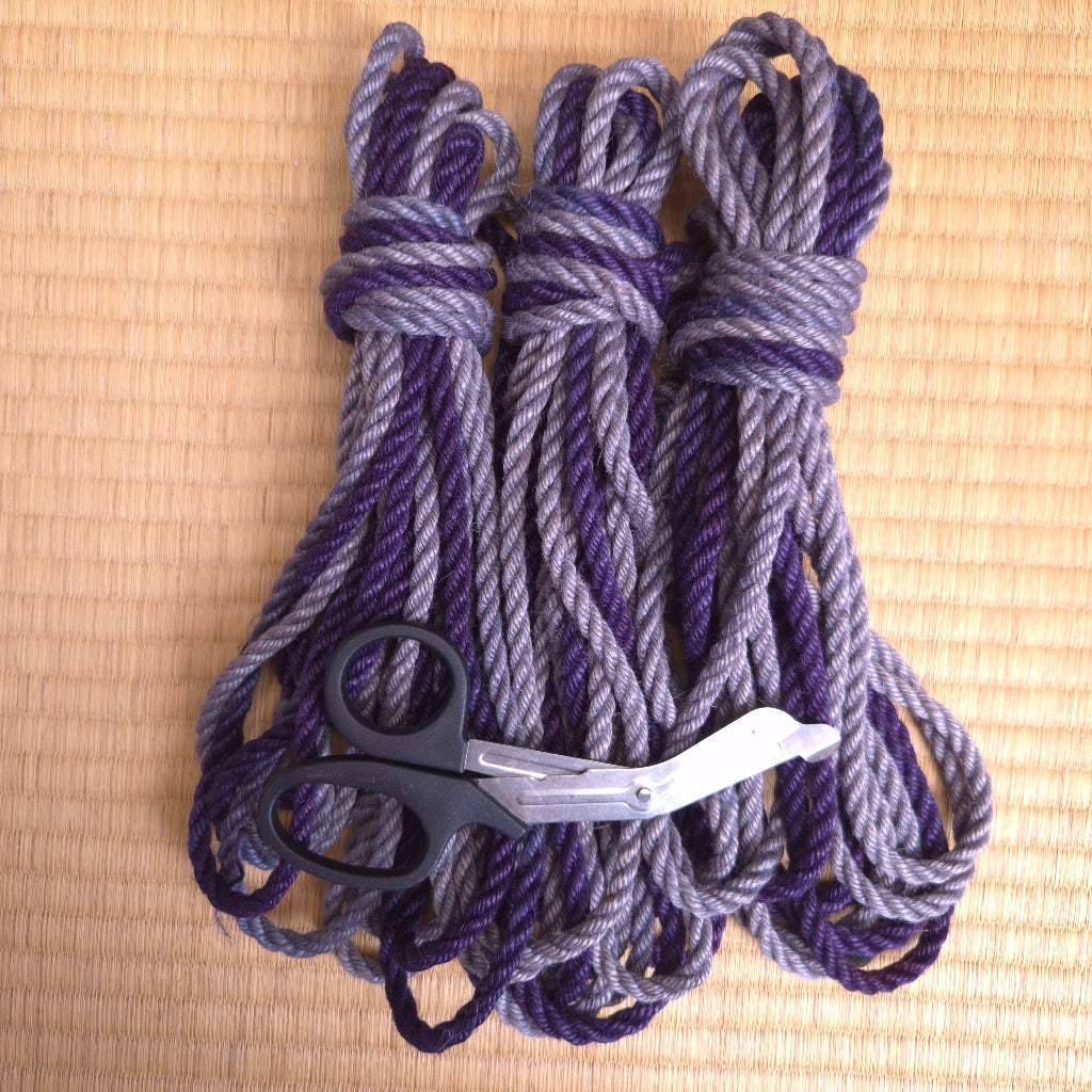Three bundles of purple and gray rope with a pair of scissors on a beige tatami mat