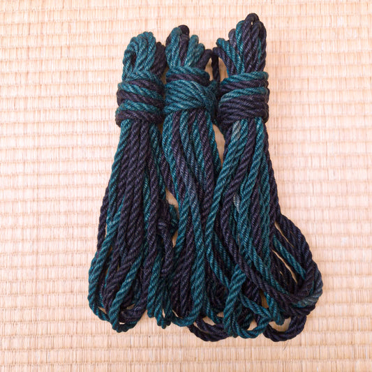 Three coiled ropes in a dark teal and black variegated pattern, tied at the top and arranged on a light beige woven mat background.