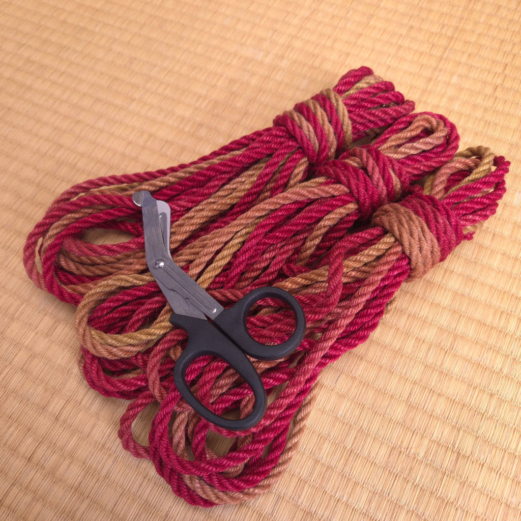 Red and brown rope with a pair of scissors on a beige woven surface